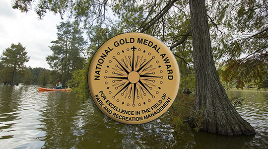 Gold Medal seal in front of people kayaking on a pond