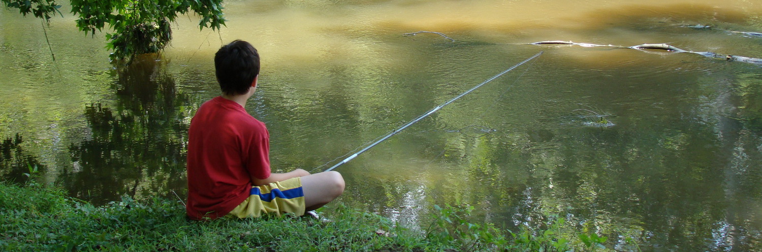 Boy sitting on the banks of Brandywine Creek with a fishing pole