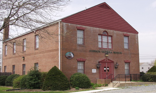 exterior view of Johnson Victrola museum. It's a large 2 story building with a red roof and red front door